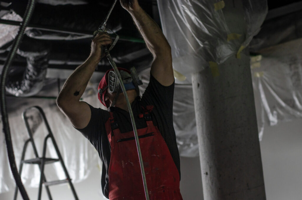 The man in the protective form paints the ceiling from the spray gun
