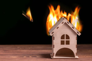 Cardboard house on fire with flames coming off the roof--indicates a house fire