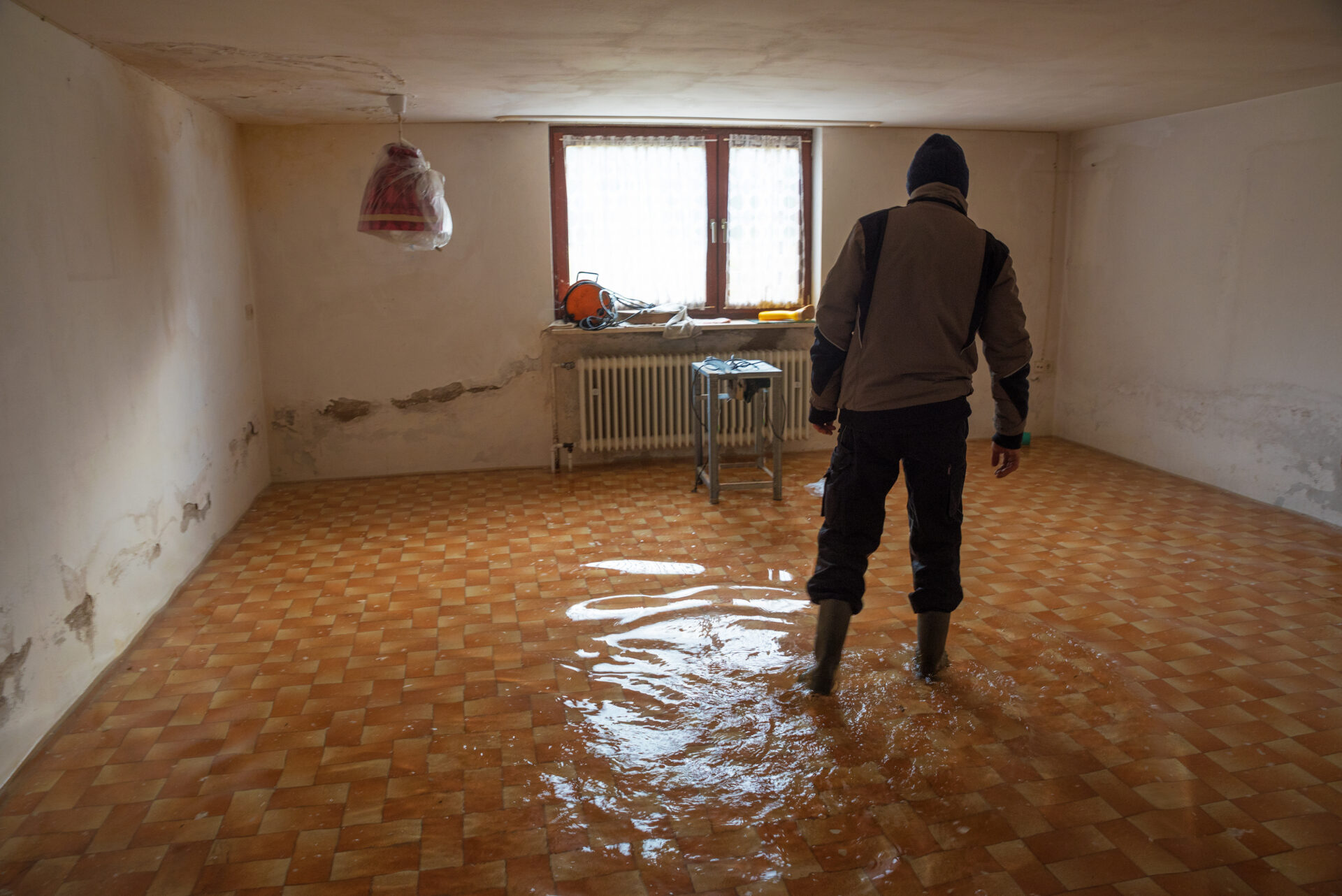 Man walks around his flooded basement with rubber boots on.