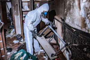 a fire damage restoration specialist in a protective suit cleans a house destroyed by a fire.